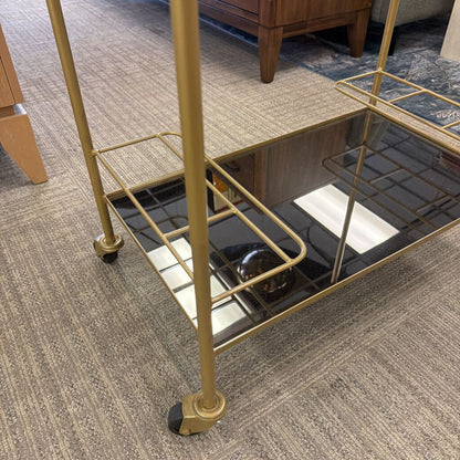 Gold metal bar cart with glass shelves on a carpeted floor