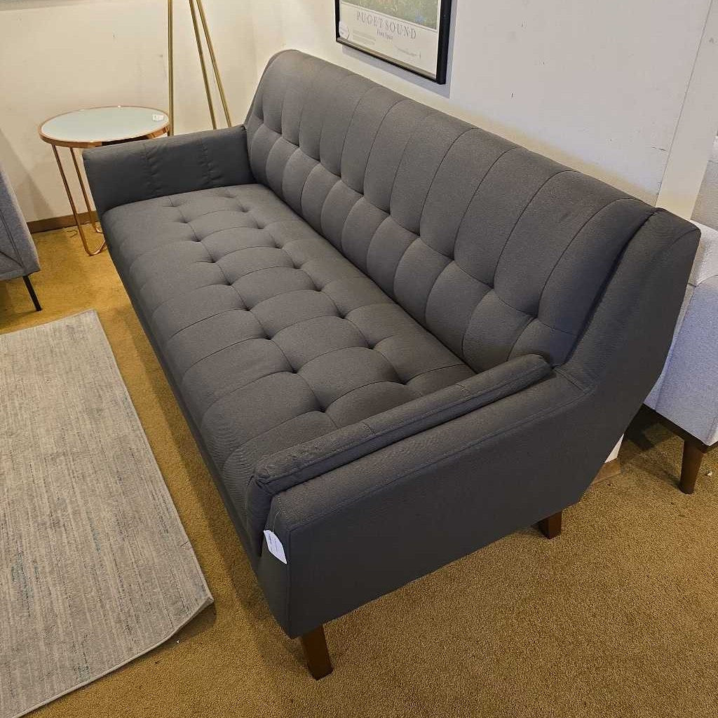 Gray tufted sofa in a room with a rug and small table.