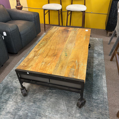 Wooden coffee table with metal legs on a gray rug in a room with furniture and decor.
