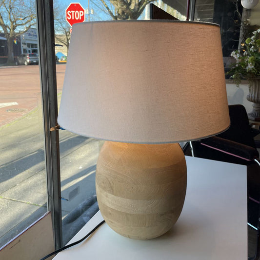 Table lamp with beige base and shade on a surface near a window with a stop sign outside.