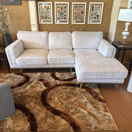Beige sectional sofa in a living room with a patterned rug and framed artwork on the wall.