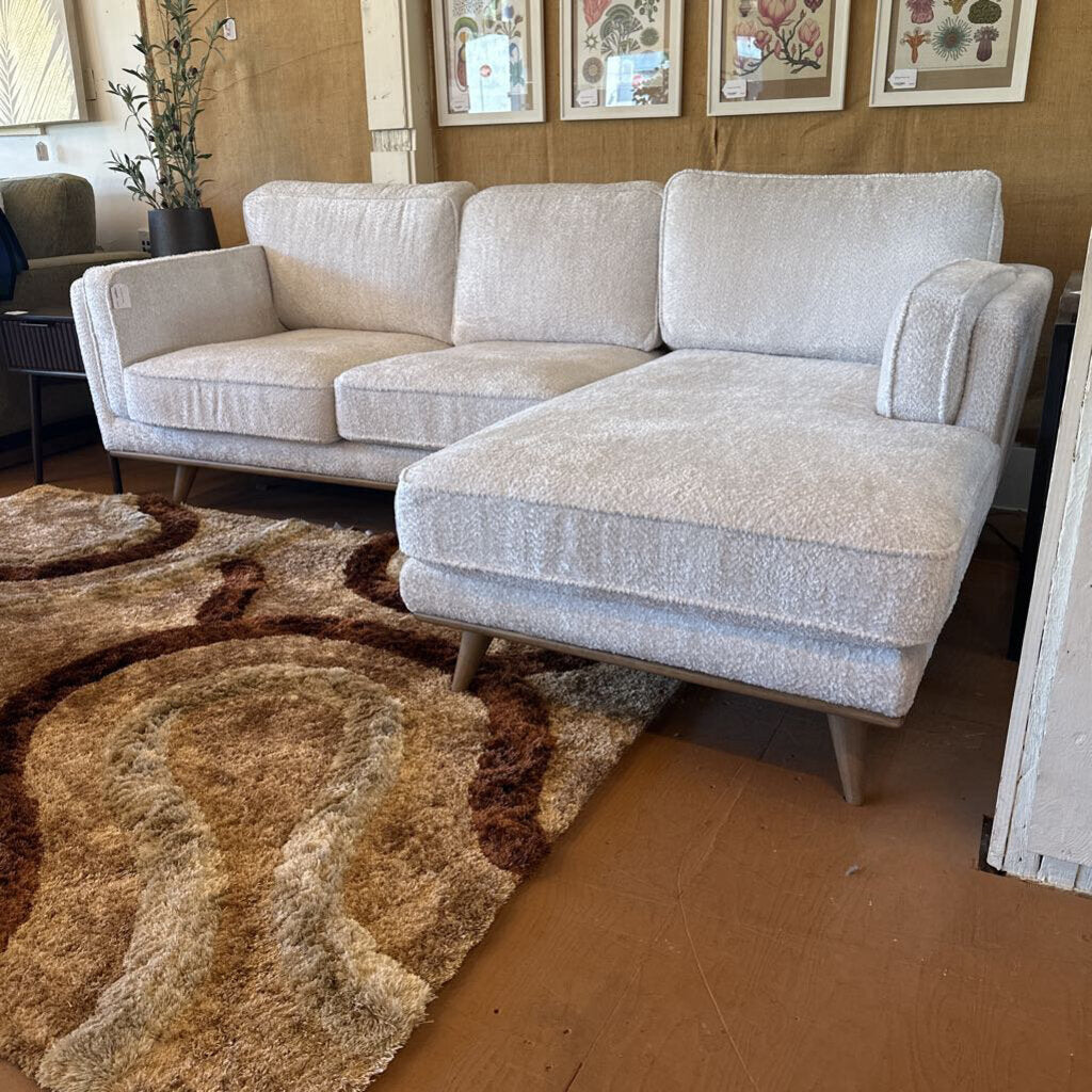 Gray sectional sofa in a room with a patterned rug and framed pictures on the wall.