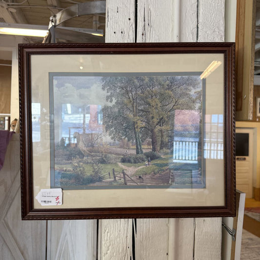 Framed print of a landscape scene with trees and a path, displayed indoors.