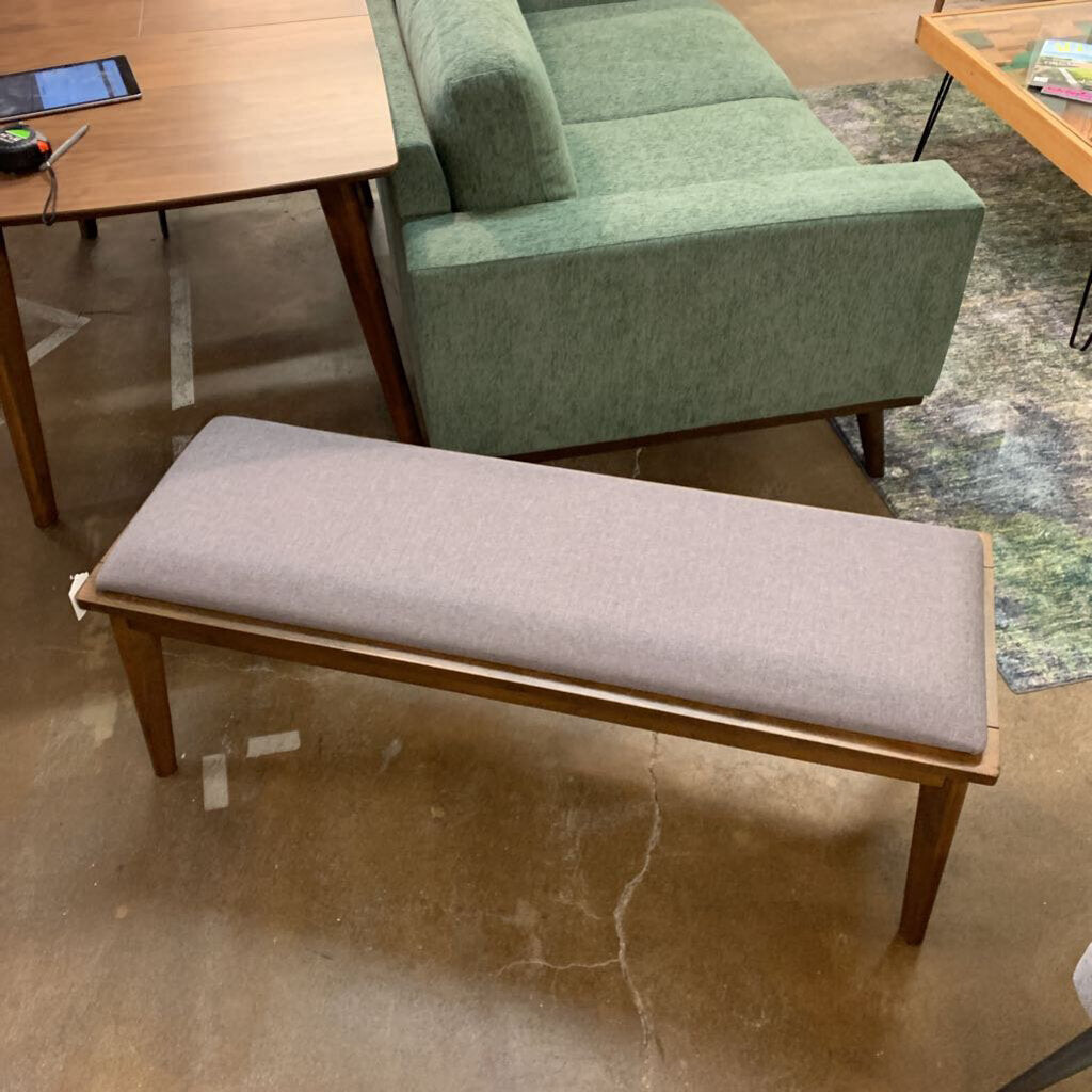 Gray upholstered bench with wooden frame in a room with a green sofa and table.