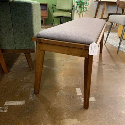 Wooden bench with gray cushion on a stone floor in a store setting