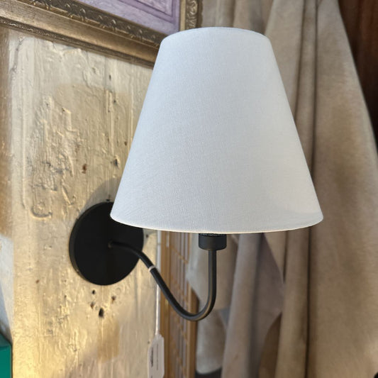Wall-mounted lamp with white shade and black fixture against a textured wall.