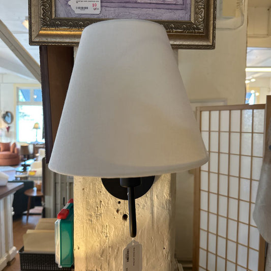White lampshade on a wall-mounted fixture with a blurred indoor background