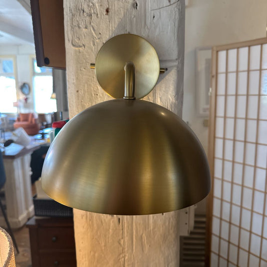 Gold wall-mounted lamp in a room with a window and door in the background