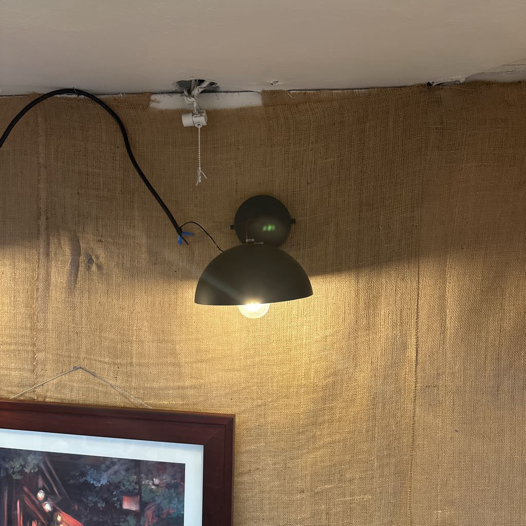 Black wall-mounted lamp on a textured brown wall with a framed picture below.