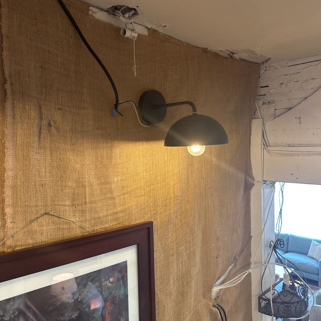 Wall-mounted light fixture on a textured wall with a painting and living room in the background.