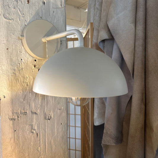 White wall-mounted lamp with a textured wall and draped fabric in the background