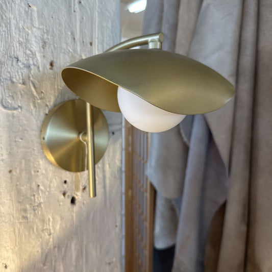 Gold wall-mounted lamp on a textured wall with a curtain in the background