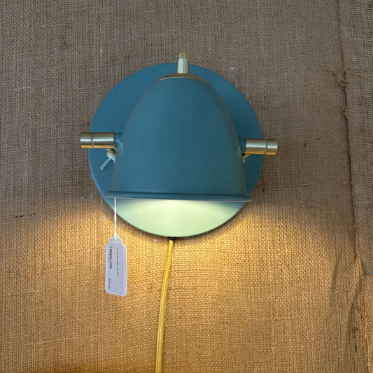 Teal wall light fixture with yellow cord on a textured brown background