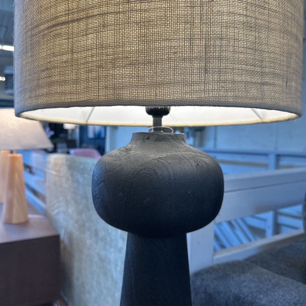 Close-up of a lamp with a textured shade and dark base in an indoor setting.