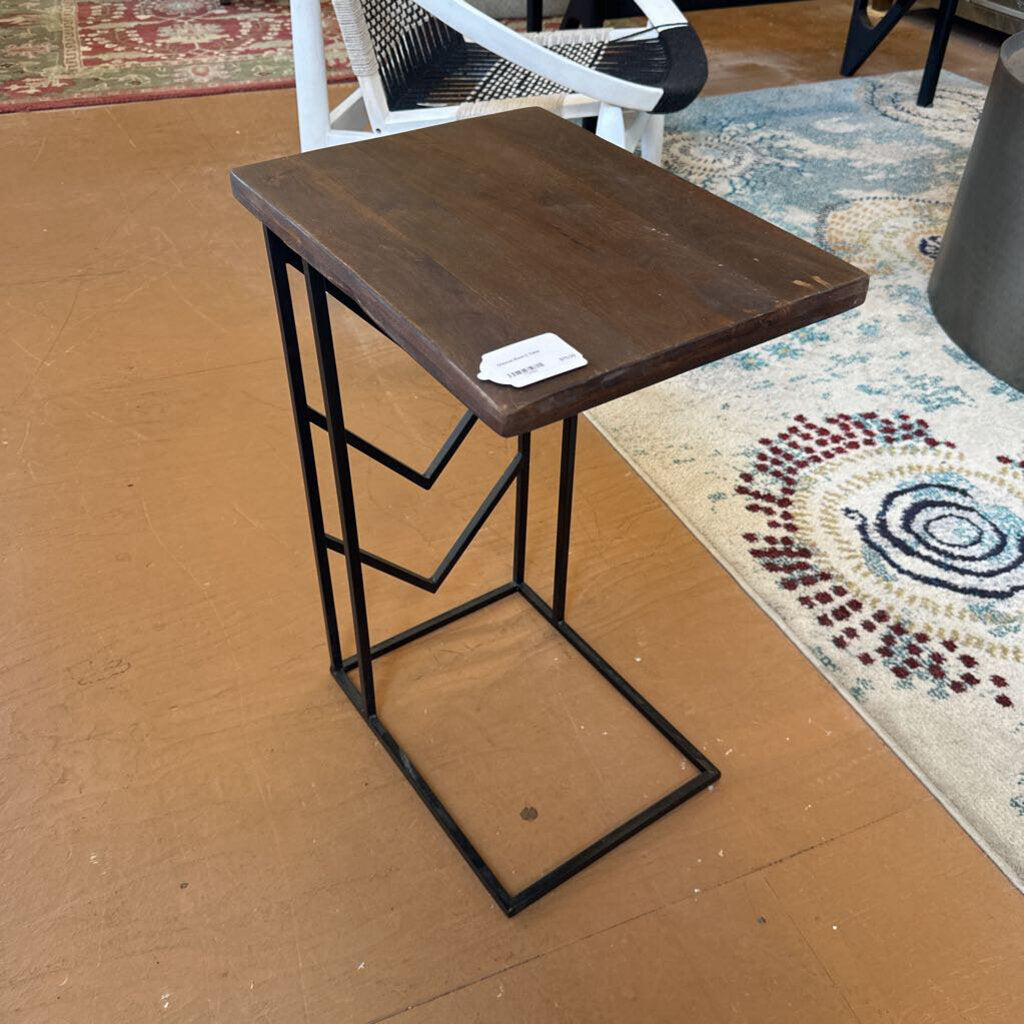 Small wooden table with metal legs on a brown floor with a patterned rug.