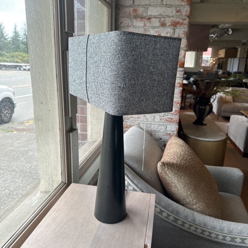 Modern lamp with a gray shade on a table next to a window with a view of a street.