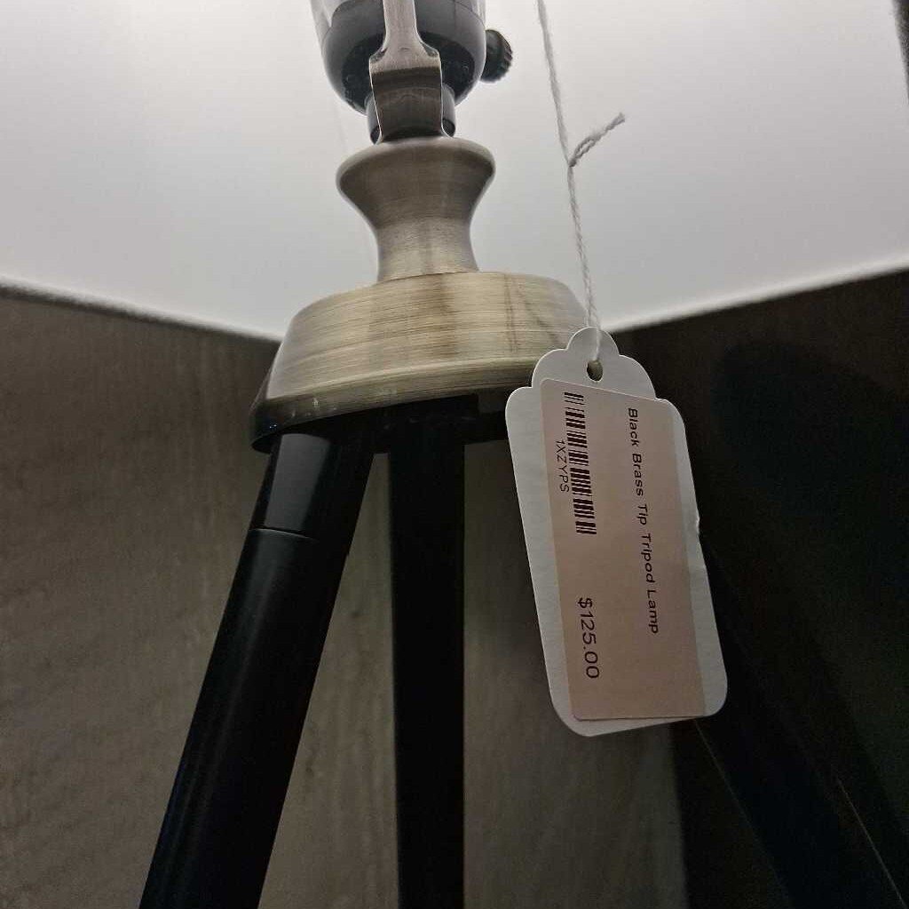 Black tripod lamp with a price tag on a neutral background