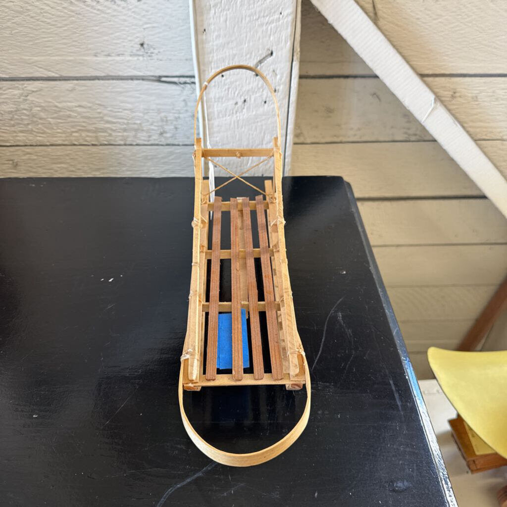 Small wooden sled with a blue object on a black surface against a wooden wall.