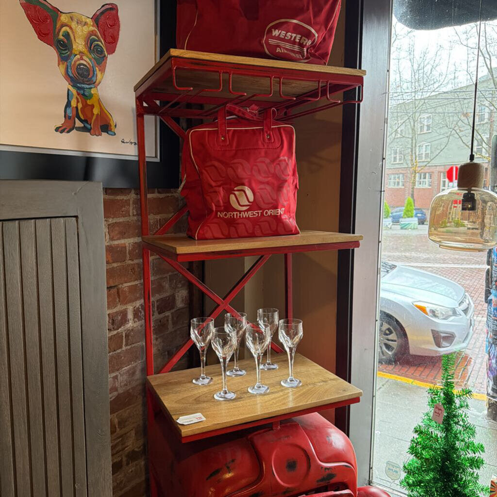 Red bag on a shelf with wine glasses below, near a window with a view of a street.