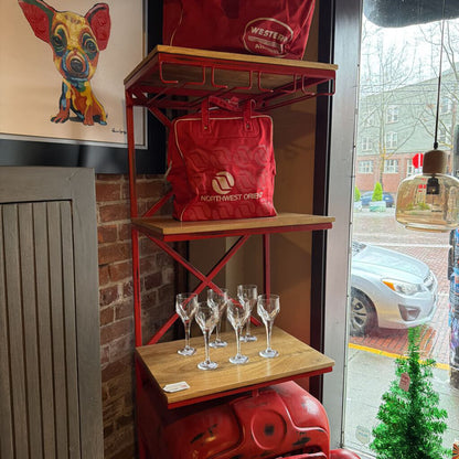Red bag on a shelf with wine glasses below, near a window with a view of a street.