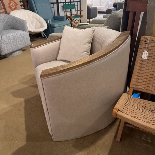 Beige armchair with wooden armrests in a showroom setting with other furniture.