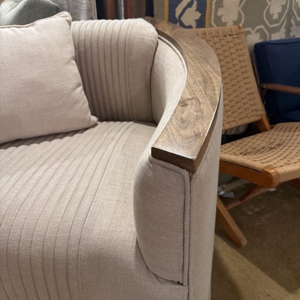 Beige sofa with a wooden armrest in a room with wicker chair and patterned wallpaper.