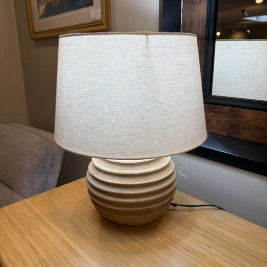 Beige textured lamp with a white shade on a wooden table.