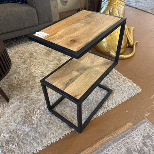 Two-tiered wooden side table with black metal frame on a carpeted floor.