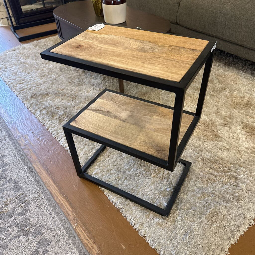 Two-tiered wooden side table with black metal frame on a beige rug.