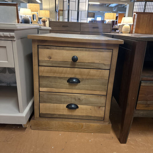 Wooden dresser with three drawers and black handles in a store setting.