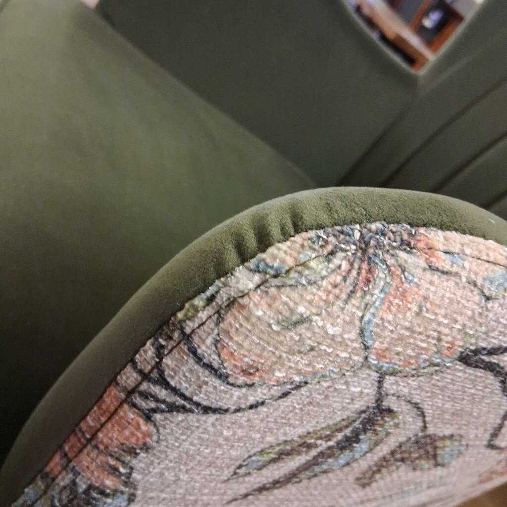 Close-up of a green cushion with floral embroidery on a chair.