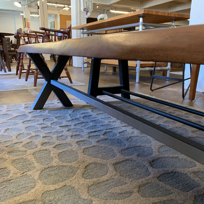 Wooden table with metal legs on a stone-patterned floor in a room with chairs and tables.