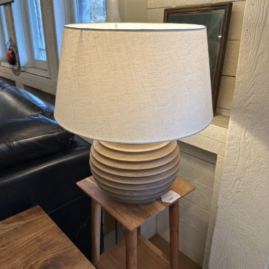 Lamp with a textured base and white shade on a small wooden table in a room.