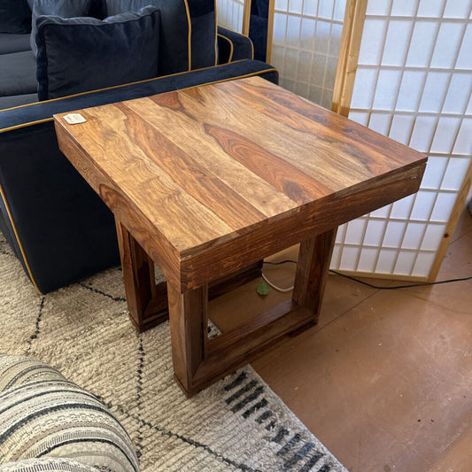 Wooden coffee table in a room with a black sofa and patterned rug.