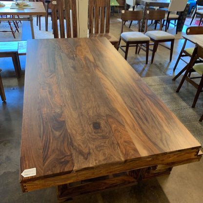 Wooden dining table in a showroom setting with chairs and tables in the background.