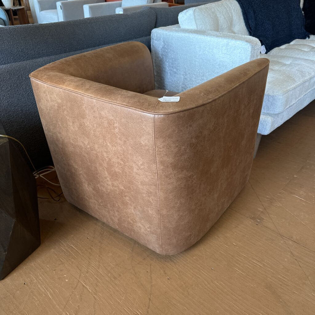 Brown leather armchair in a showroom setting with other furniture.