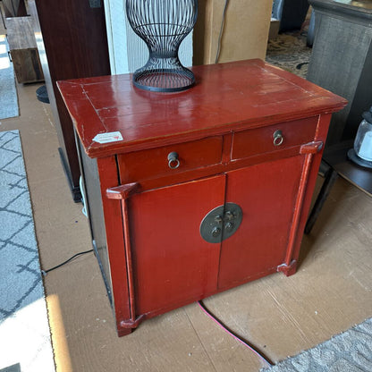 Red cabinet with a decorative handle on a cardboard surface