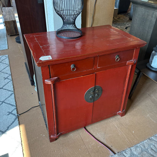 Red cabinet with a decorative handle on a cardboard surface