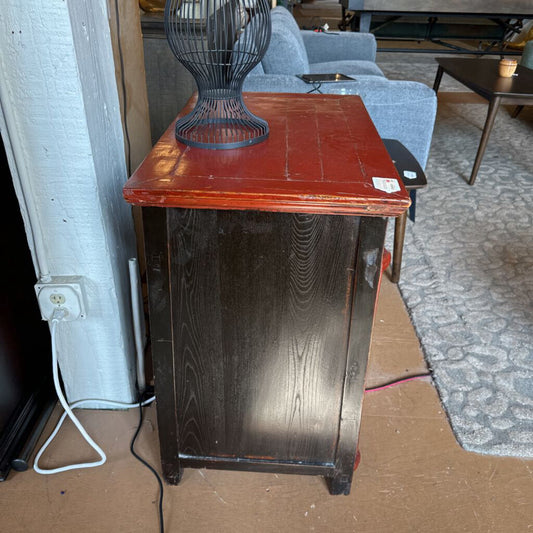 Wooden side table with a red top and black wire basket on top, in an indoor setting.