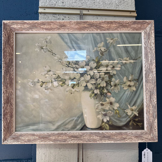 Framed artwork of a floral arrangement in a white vase on a textured surface.