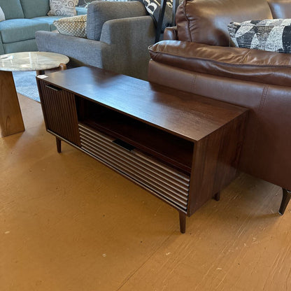 Wooden TV stand in a living room with brown leather sofa and gray sofa in the background.