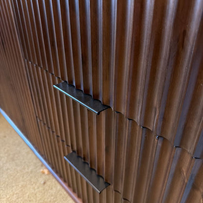 Close-up of a wooden cabinet with ribbed design and metal handles.