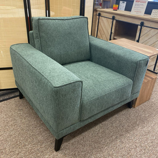 Green armchair in a store setting with a wooden floor and furniture in the background.