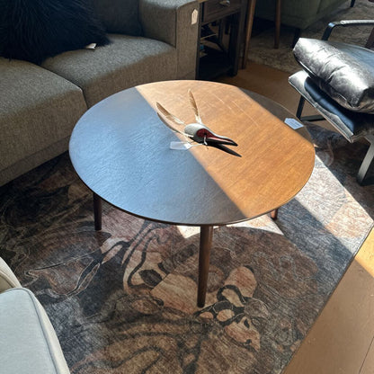 Round coffee table with a wooden top and black base in a living room setting.