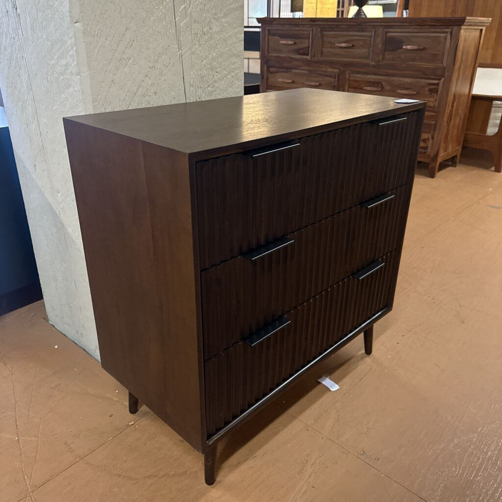 Wooden dresser with three drawers on a brown floor.