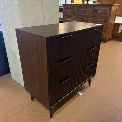 Wooden dresser with three drawers on a brown floor.