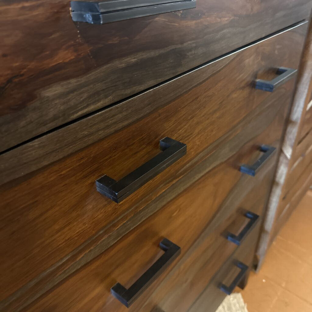 Wooden dresser with black metal handles on a wooden floor.
