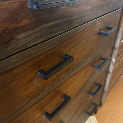Wooden dresser with black metal handles on a wooden floor.