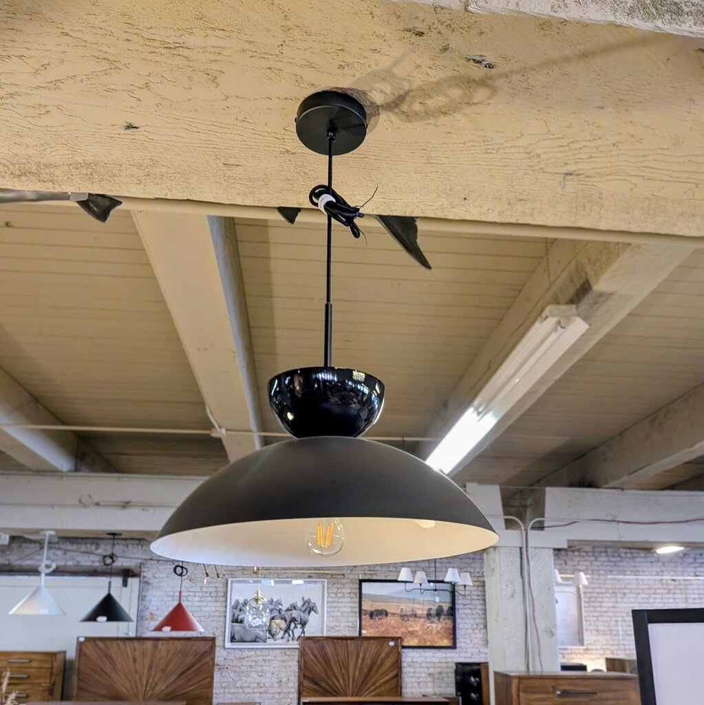 Black pendant light hanging from a wooden ceiling in an indoor setting.