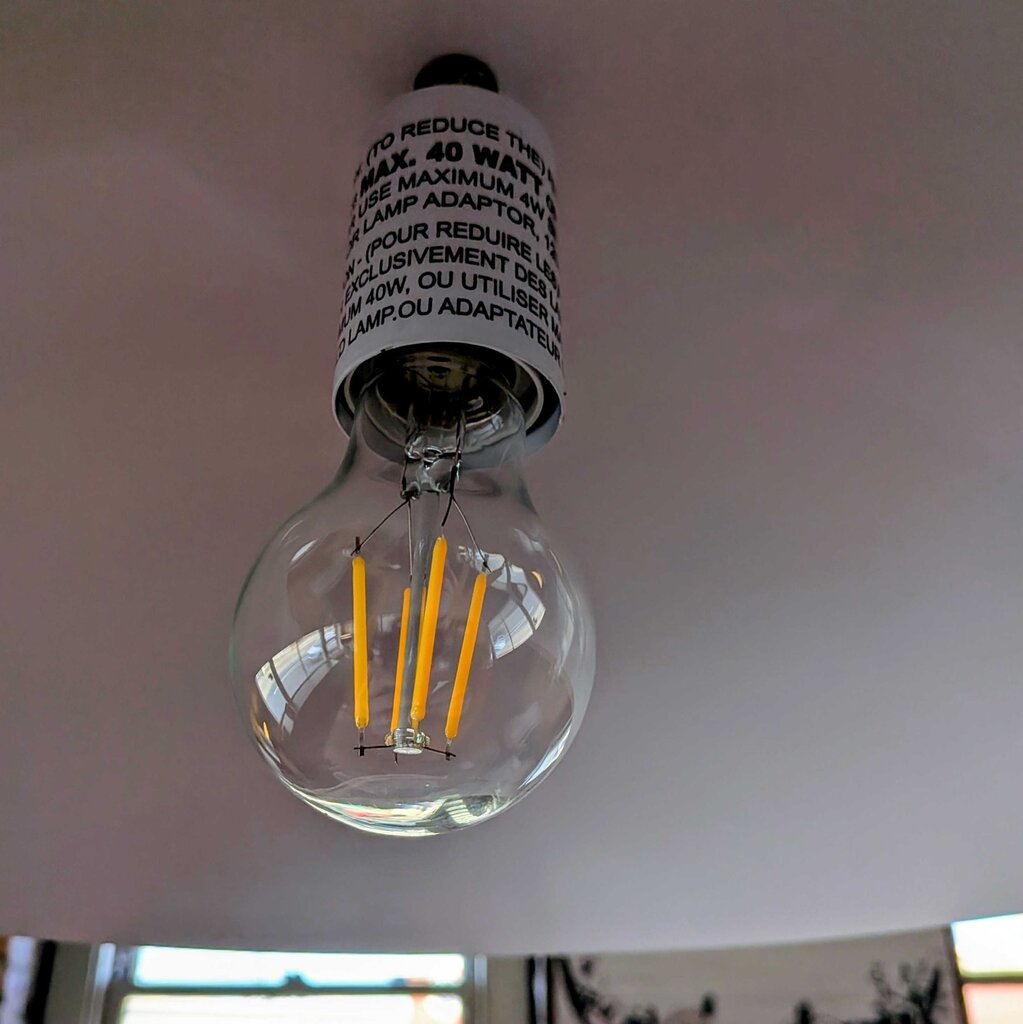 Clear LED light bulb with visible filaments on a white ceiling